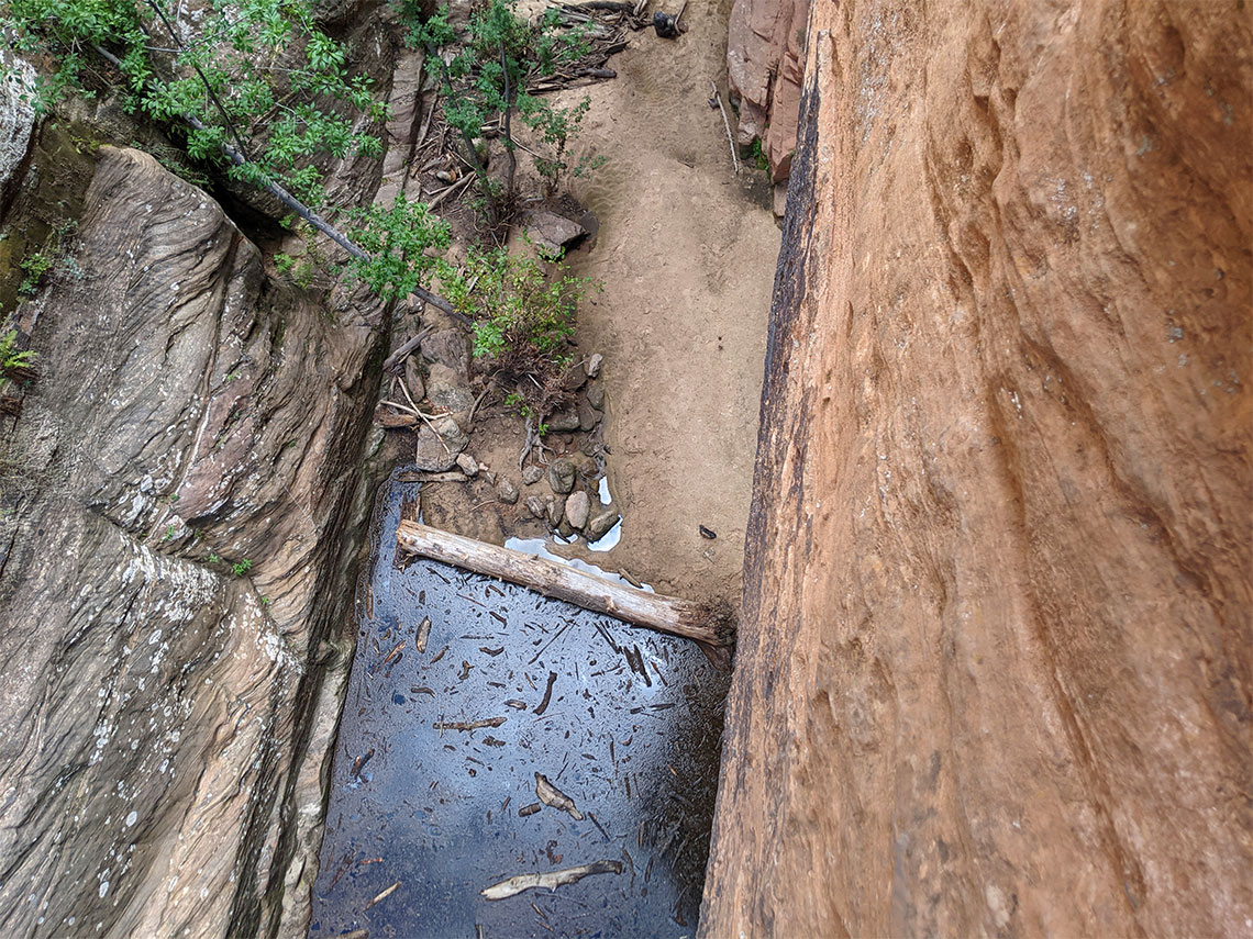 Water filled with debris at the bottom of rappel 6 in Behunin